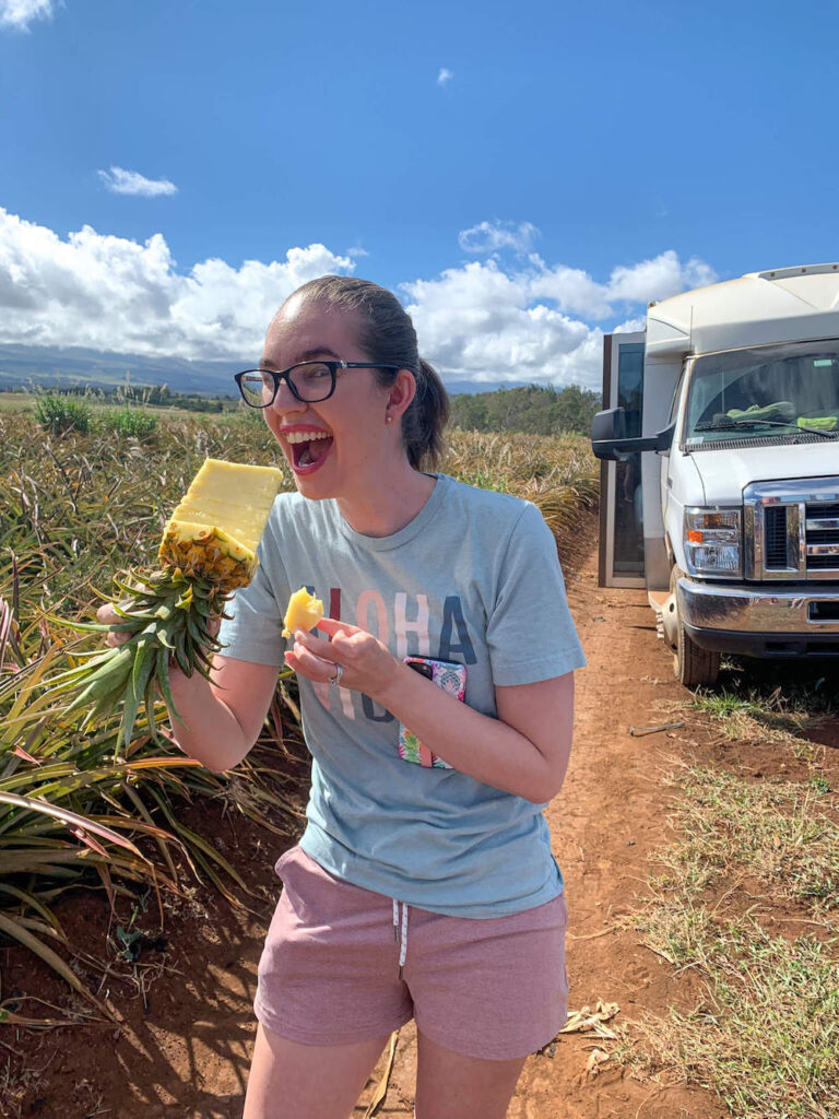 Image of a lady biting into a pineapple core in front of a van at the Maui Pineapple Tour