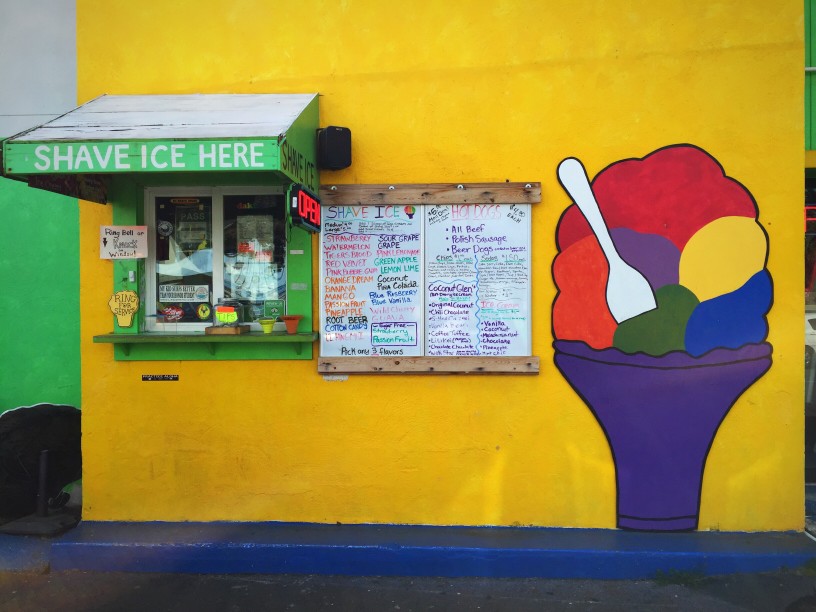 Image of a shave ice mural on a yellow wall next to a shave ice walk up window.