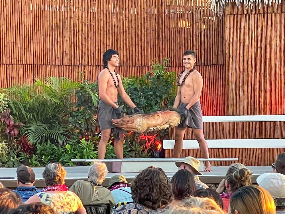 Image of two young men holding up a full roasted pig at the Royal Lahaina Luau.