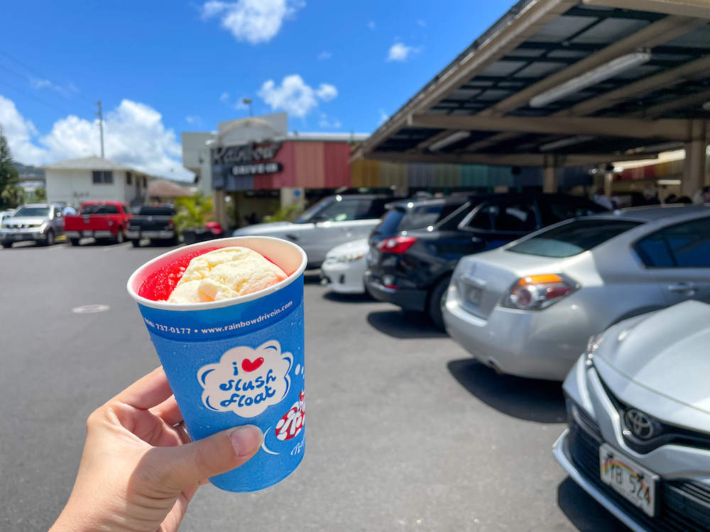 Image of someone holding up a red and white slushie in front of the Rainbow Drive In sign on Oahu.