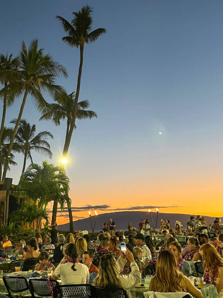 Image of a sunset on Maui at the Royal Lahaina luau with a bunch of people sitting at tables.