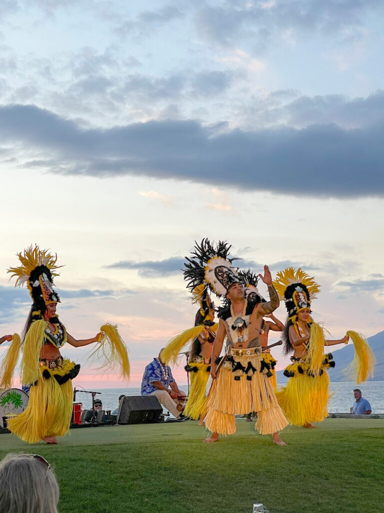 Image of a bunch of Tahitian dancers wearing yellow costumes dancing outside at sunset in Maui.