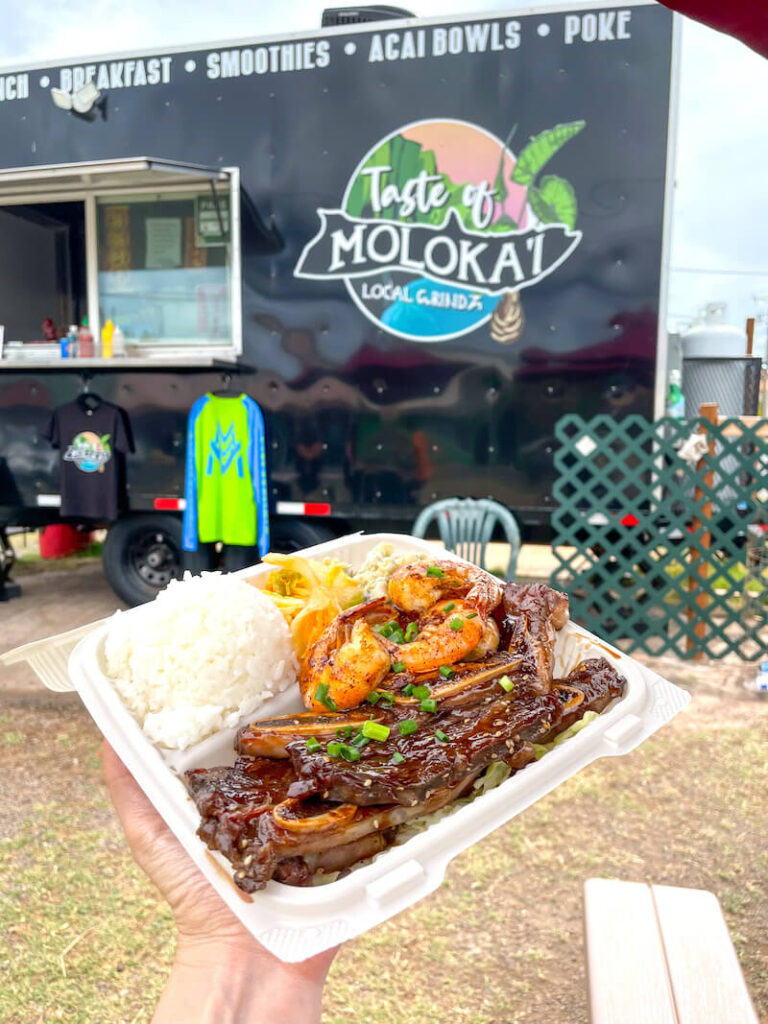 Image of a Hawaiian plate lunch with kalbi ribs, rice, macaroni salad, and garlic shrimp in front of the Taste of Moloka'i food truck.