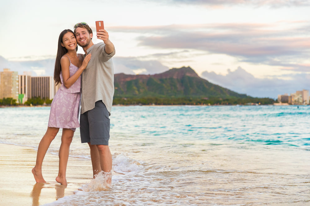 Image of a couple taking a selfie on Waikiki Beach with Diamond Head in the Background