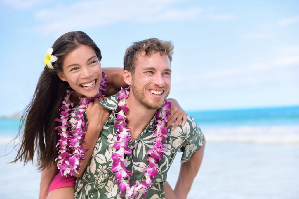 Image of a man and woman wearing purple orchid leis on the beach in Hawaii