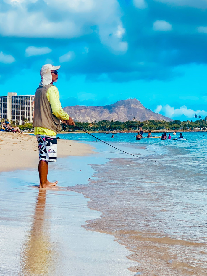 Image of a man holding a fishing rod in Waikiki Beach with Diamond Head in the Background