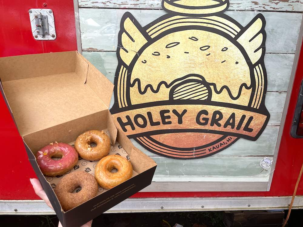 Image of a four-pack of donuts in a box in front of the Holey Grail sign on a Kauai food truck.