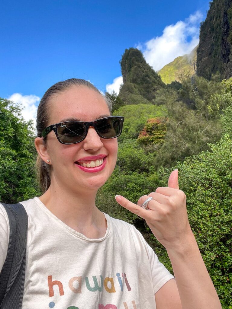 Image of a woman throwing a shaka with I'ao Needle in the background.