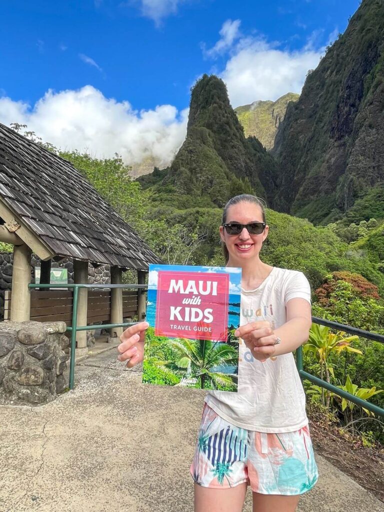 Image of a woman holding a Maui with Kids travel guide at the I'ao Needle Lookout on Maui.