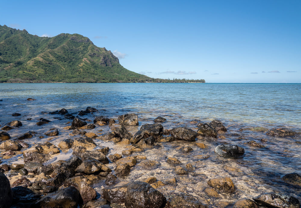 Image of rocks in the water with Koolau mountains in the background.