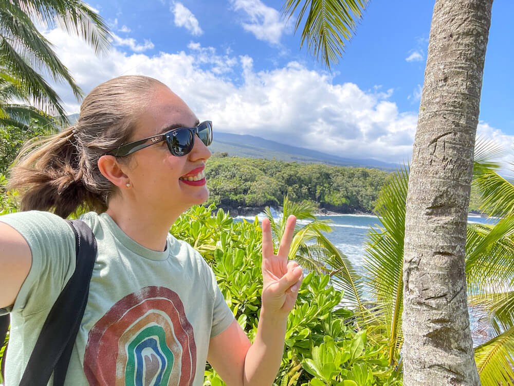 Image of a woman wearing a rainbow shirt and sunglasses taking a selfie at Kahanu Garden in Maui