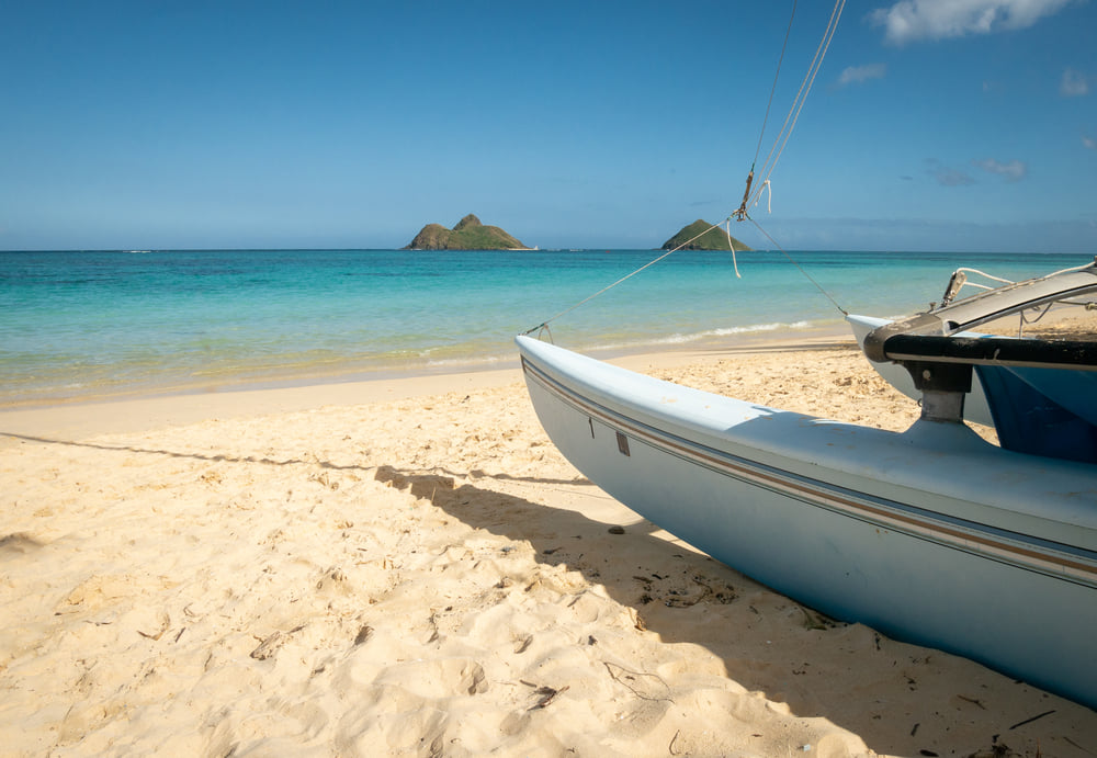 Image of a boat on a sandy beach with little islands in the background