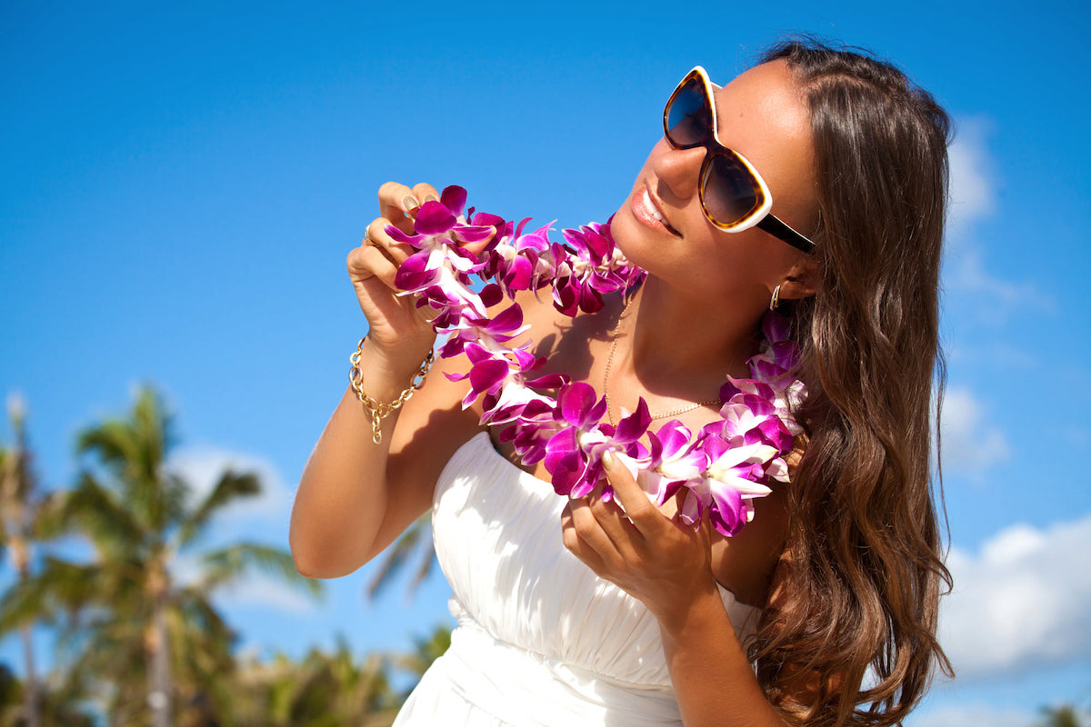 Find out how to book a lei greeting in Honolulu Oahu by top Hawaii blog Hawaii Travel with Kids! Image of a woman weraing a white dress, sunglasses, and a purple orchid lei