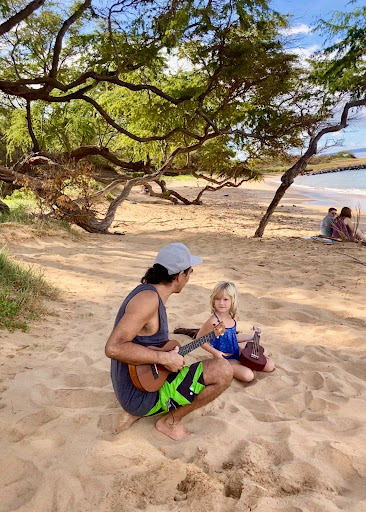 Image of a girl and a man sitting on a beach playing the ukulele