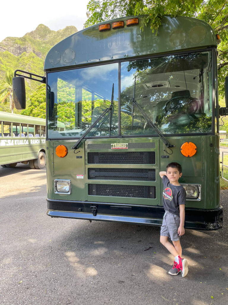 Image of a boy standing in front of a green bus at Kualoa Ranch.