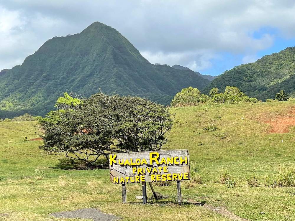 Image of the Kualoa Ranch private nature reserve sign in a valley with green mountains.