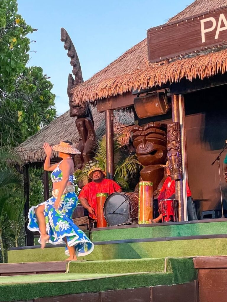 Image of a lady wearing a tropical skirt and top and hat dancing on stage.