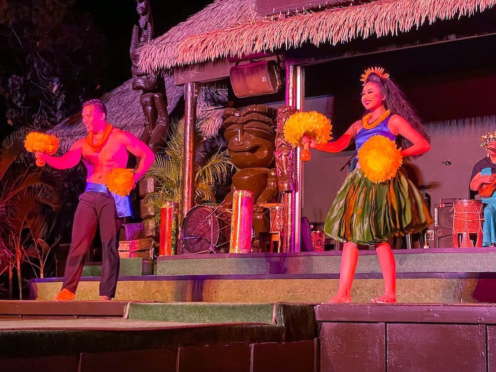 Image of a man and woman dancing with feather gourd rattles at the Paradise Cove Luau on Oahu.