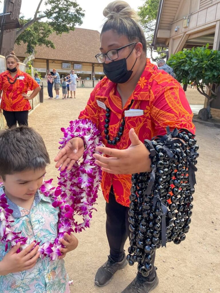 Image of a woman holding purple orchid leis and black kukui nut leis at the Paradise Cove luau on Oahu.