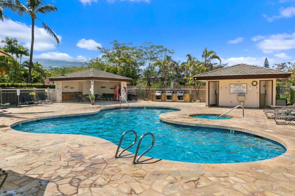 Image of a pool and hot tub with a bathroom and canopy in the background.