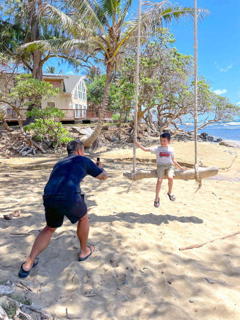 Image of a man taking a photo of a boy on a beach swing on Oahu