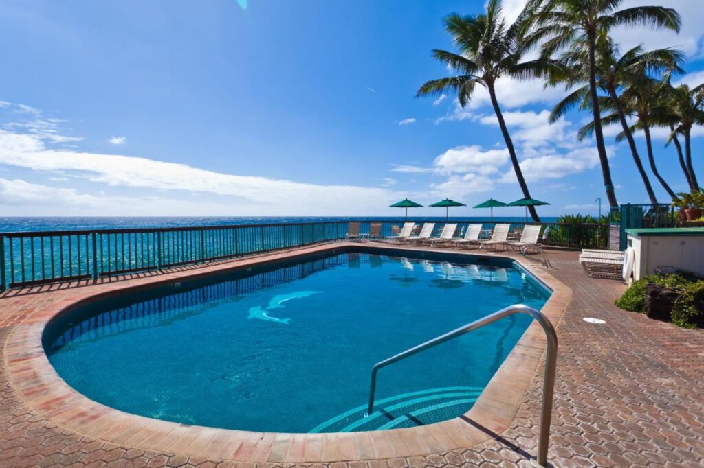 Image of a pool next the ocean with palm trees in the background