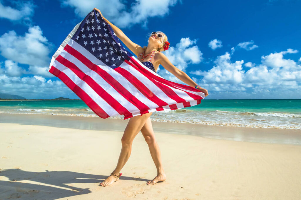 Image of a woman wearing a swimsuit holding an American flag at the beach in Hawaii