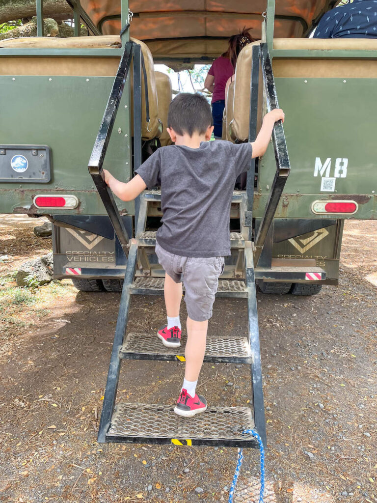 Image of a 5yo boy climbing up metal stairs into a green jeep.