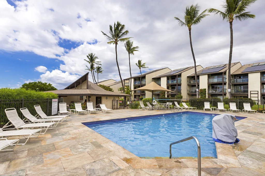 Image of a small pool surrounded by pool furniture with a condominium in the background