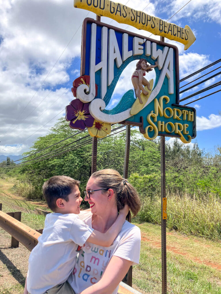 Image of a mom holding a boy in front of the Haleiwa North Shore sign