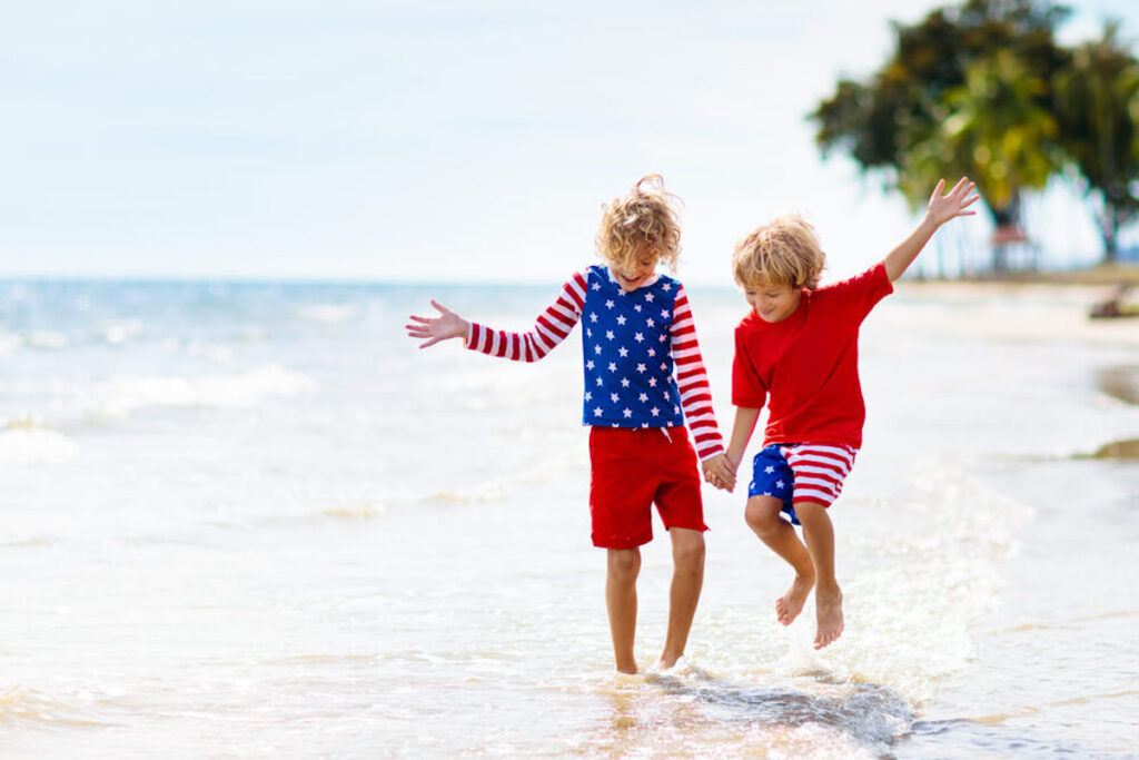 Image of two boys wearing American Flag swimsuits jumping in the water at a beach in Hawaii