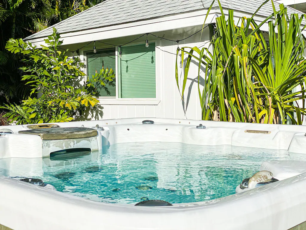 Image of a hot tub in front of a white house with tropical leaves