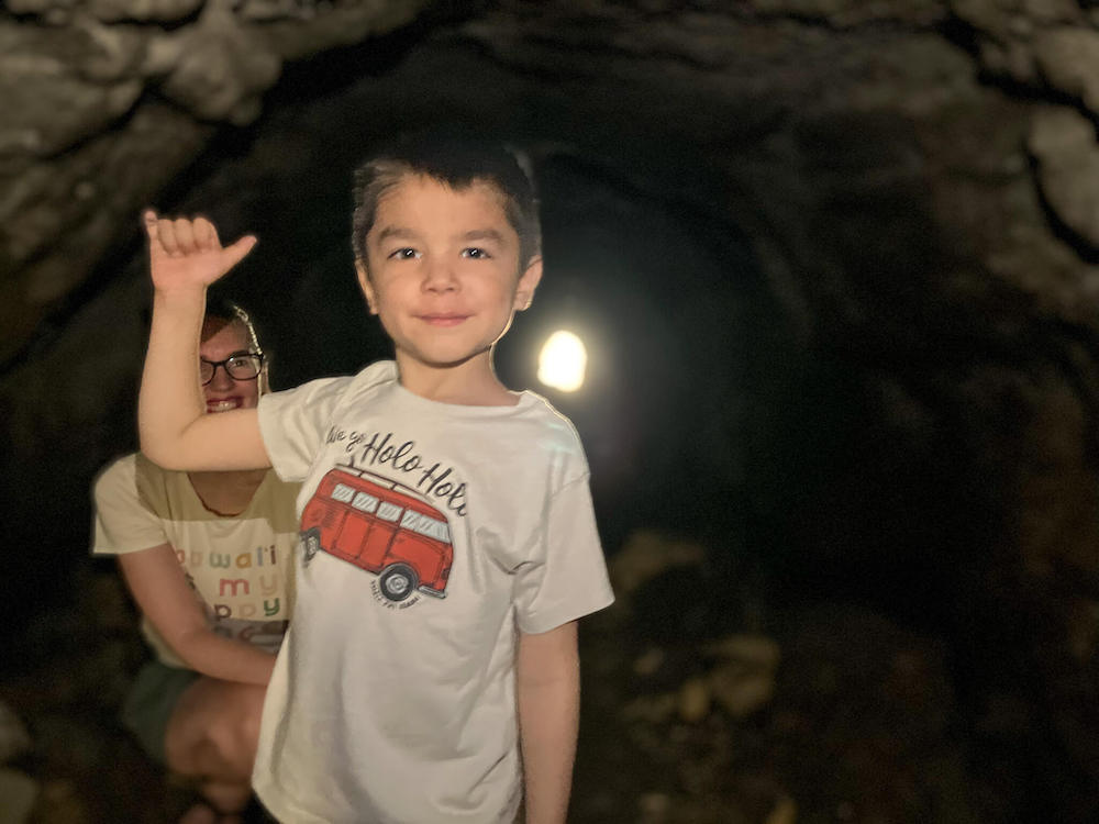 Image of a boy waving a shaka inside a dark lava tube on Oahu