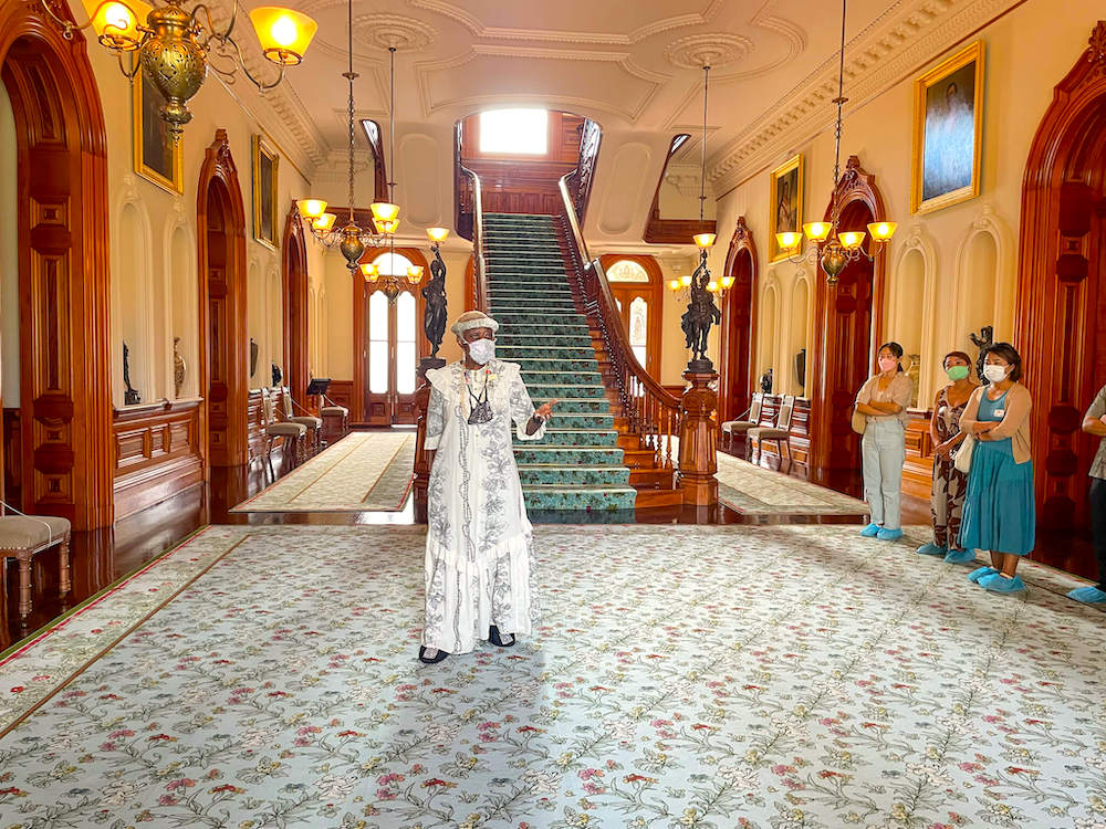 Image of a lady wearing a long white muumuu inside Iolani Palace.