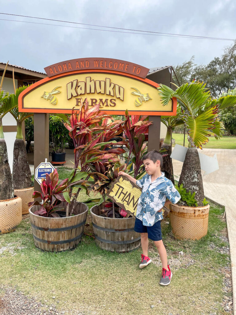 Image of a boy standing in front of the Kahuku Farms sign