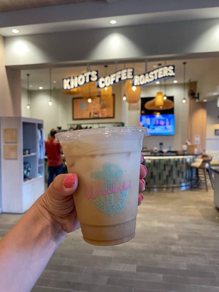 Image of a takeaway coffee cup in front of the Knots Coffee Roasters sign at the Queen Kapiolani Hotel in Waikiki Oahu.