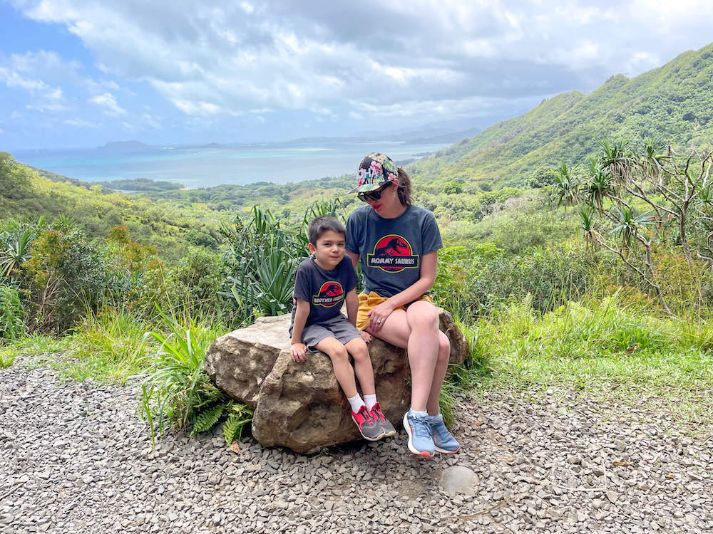 Image of a mom and son wearing Jurassic Park shirts sitting a big rock at Kualoa Ranch.