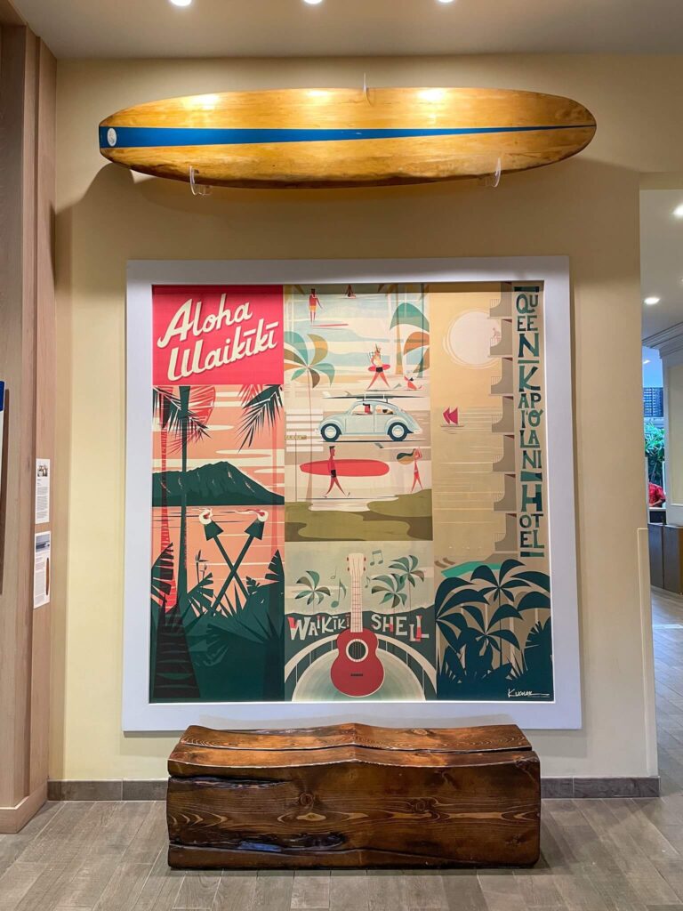 Image of a large Hawaiian artwork with a wooden bench in front at the Queen Kapiolani Hotel in Waikiki.