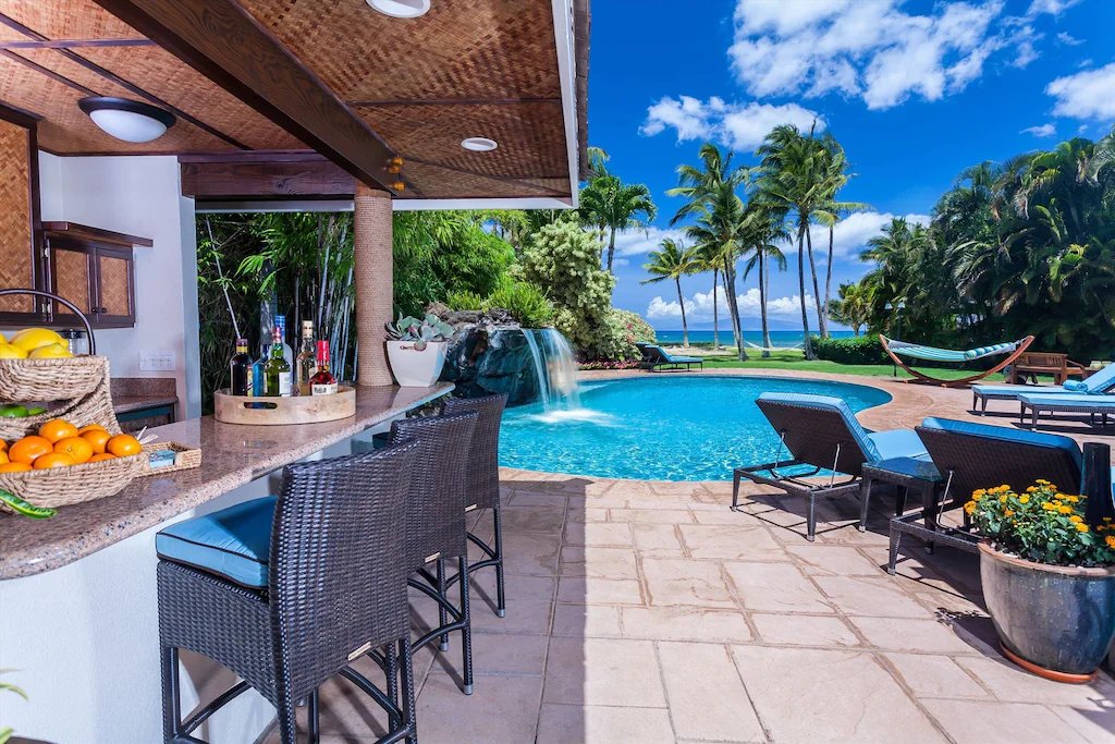 Image of a pool with a little waterfall, a hammock, and and outdoor bar area at a Maui villa