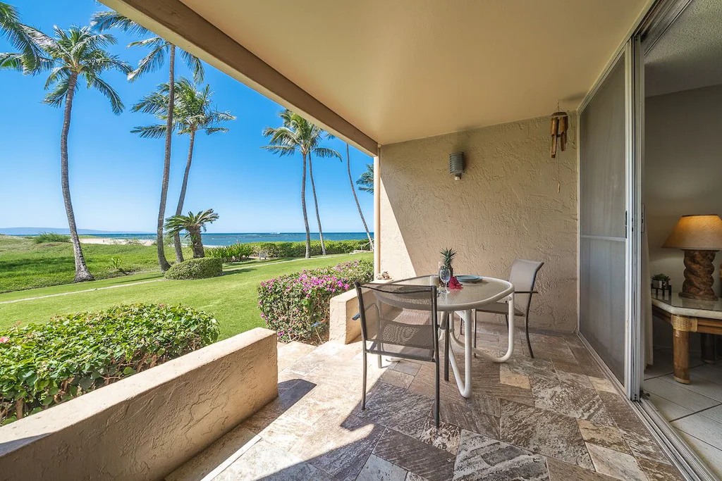 image of a covered patio with a table and chairs in front of a grassy lawn by the beach