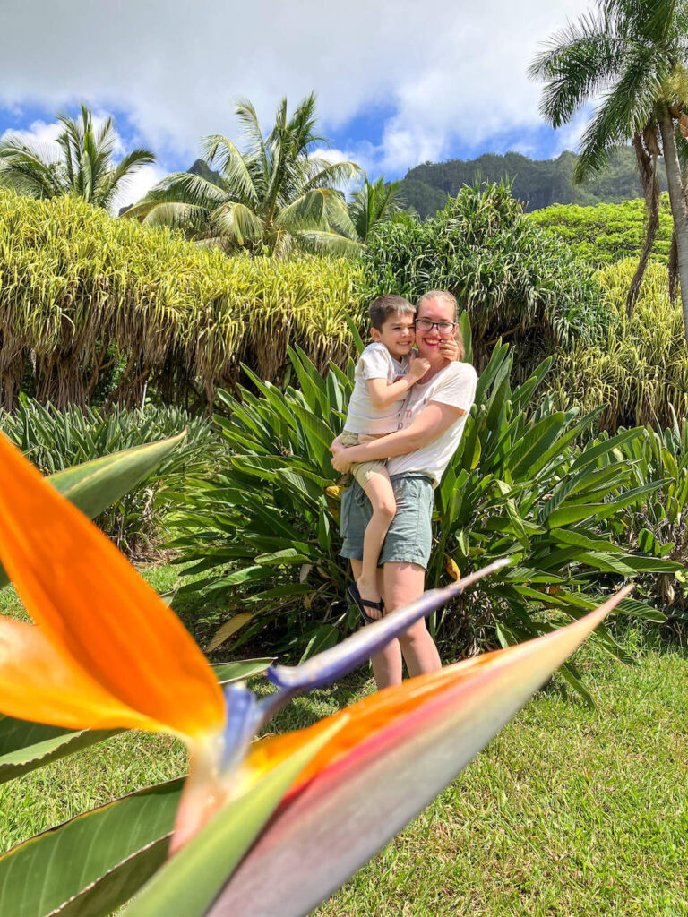 Image of a mom holding a 5yo boy in a lush garden with a bird of paradise flower in the foreground