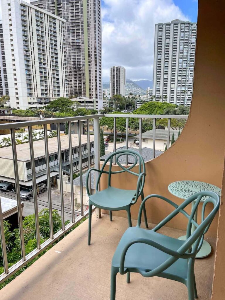 Image of two green chairs and a green table on a lanai at the Queen Kapiolani Hotel on Oahu.