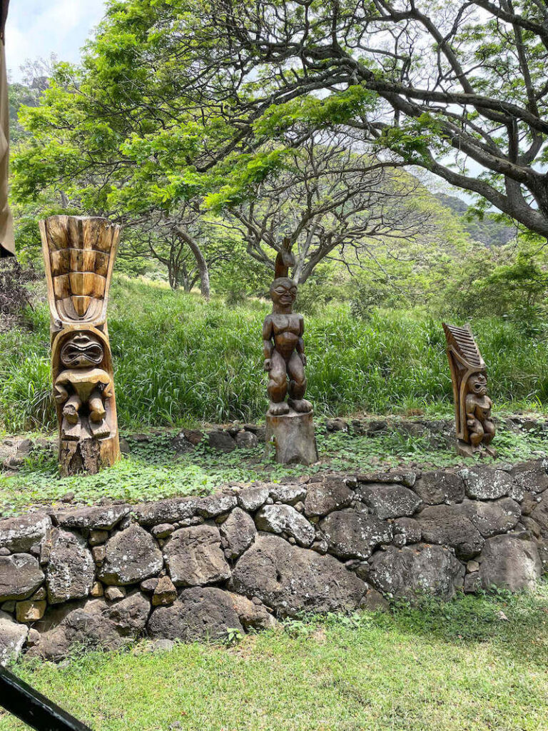 Image of 3 tiki statues on a grassy platform with lava rocks at Kualoa Ranch.