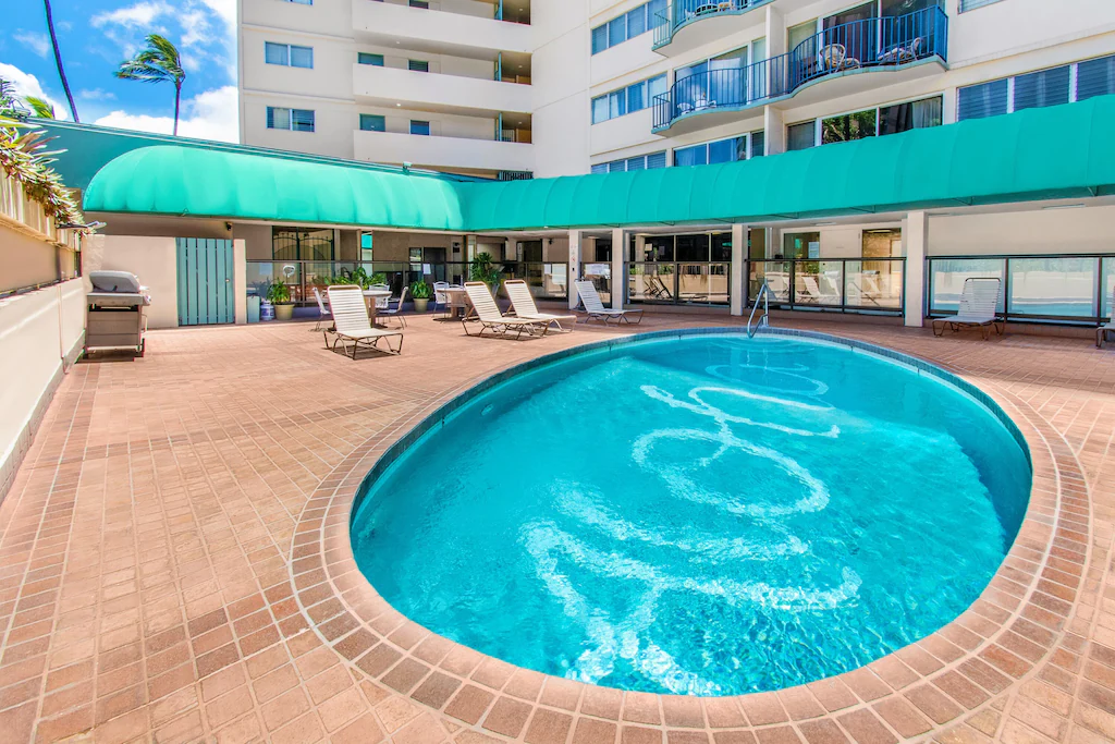 Image of an oval pool that says Aloha at the bottom with a tall building in the background