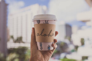 Find our where to get the best coffee in Waikiki recommended by top Hawaii blog Hawaii Travel with Kids! Image of a takeaway cup that has Aloha written on it