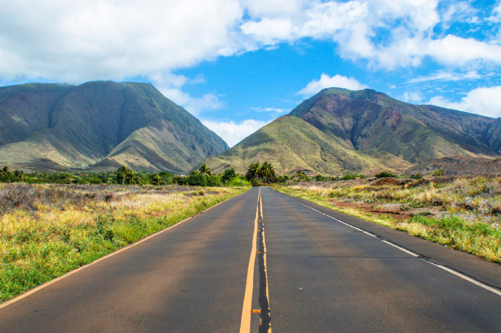 Check out this guide to getting around Maui without a car by top Hawaii blog Hawaii Travel with Kids. Image of an empty road leading toward the mountains on Maui