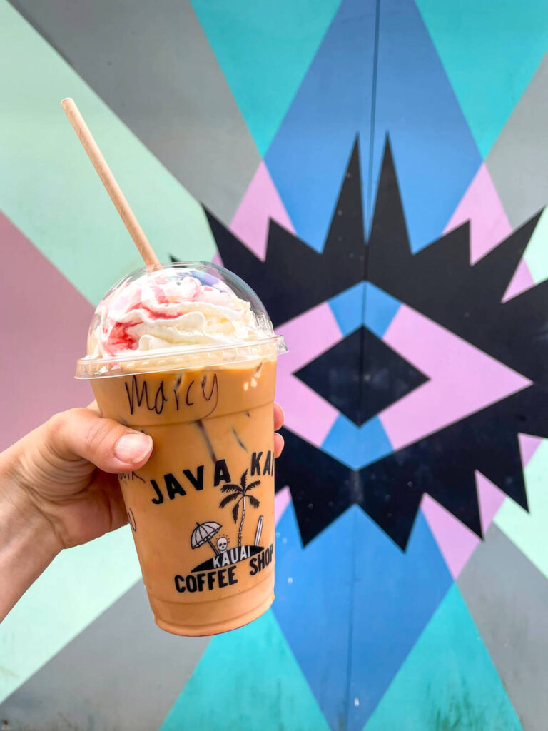 Image of an iced coffee from Java Kai on Kauai in front of a painted mural