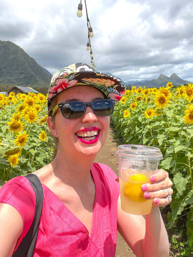 Image of a woman in a pink dress holding a cup of lemonade in a Hawaii sunflower field