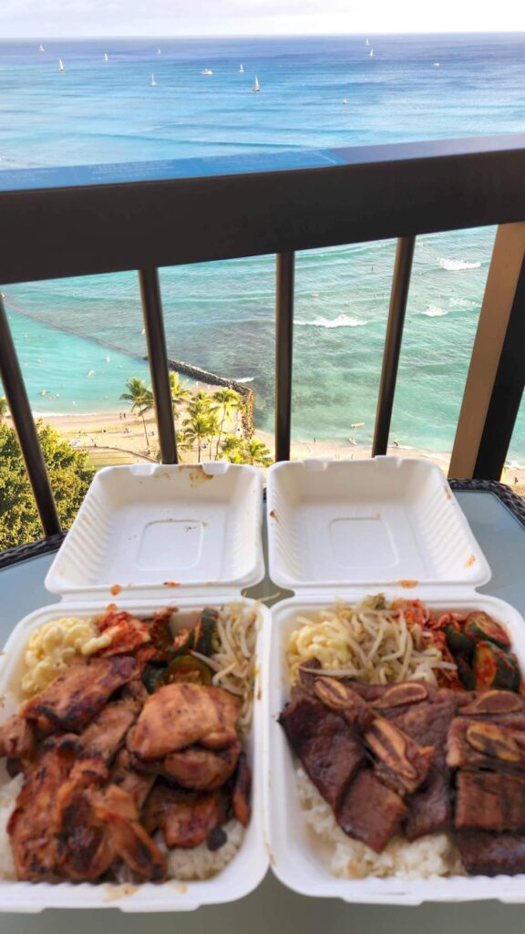 Image of takeout containers from Me's BBQ on a lanai in front of the ocean