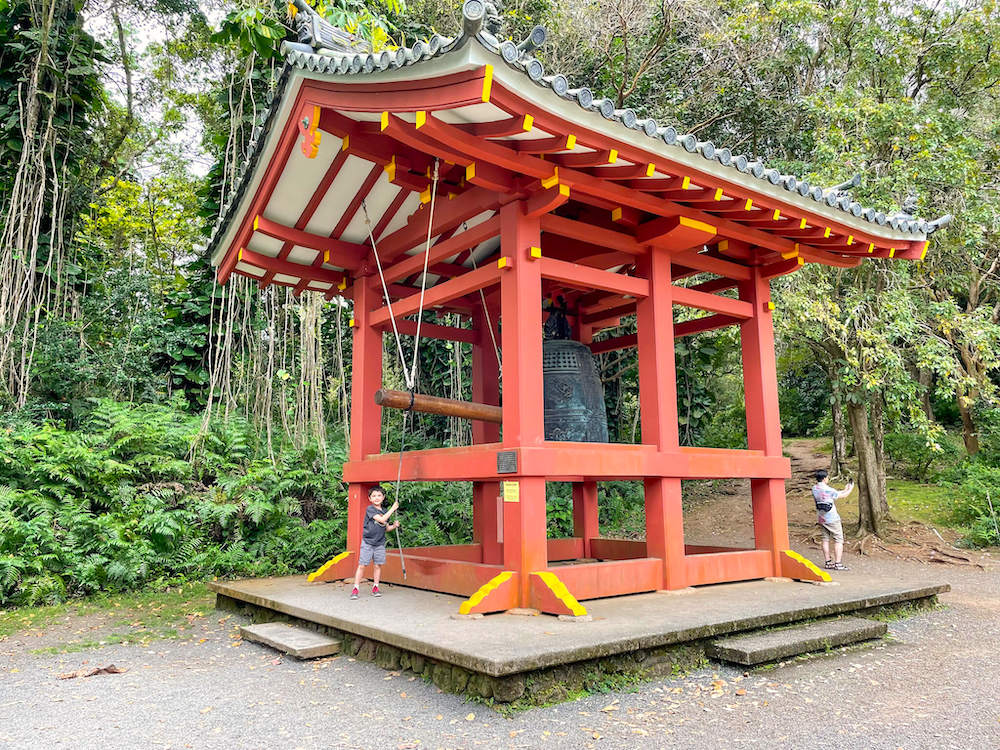 Image of a boy ringing a massive bell inside a red Asian-style structure at the Byodo-In Temple in Hawaii